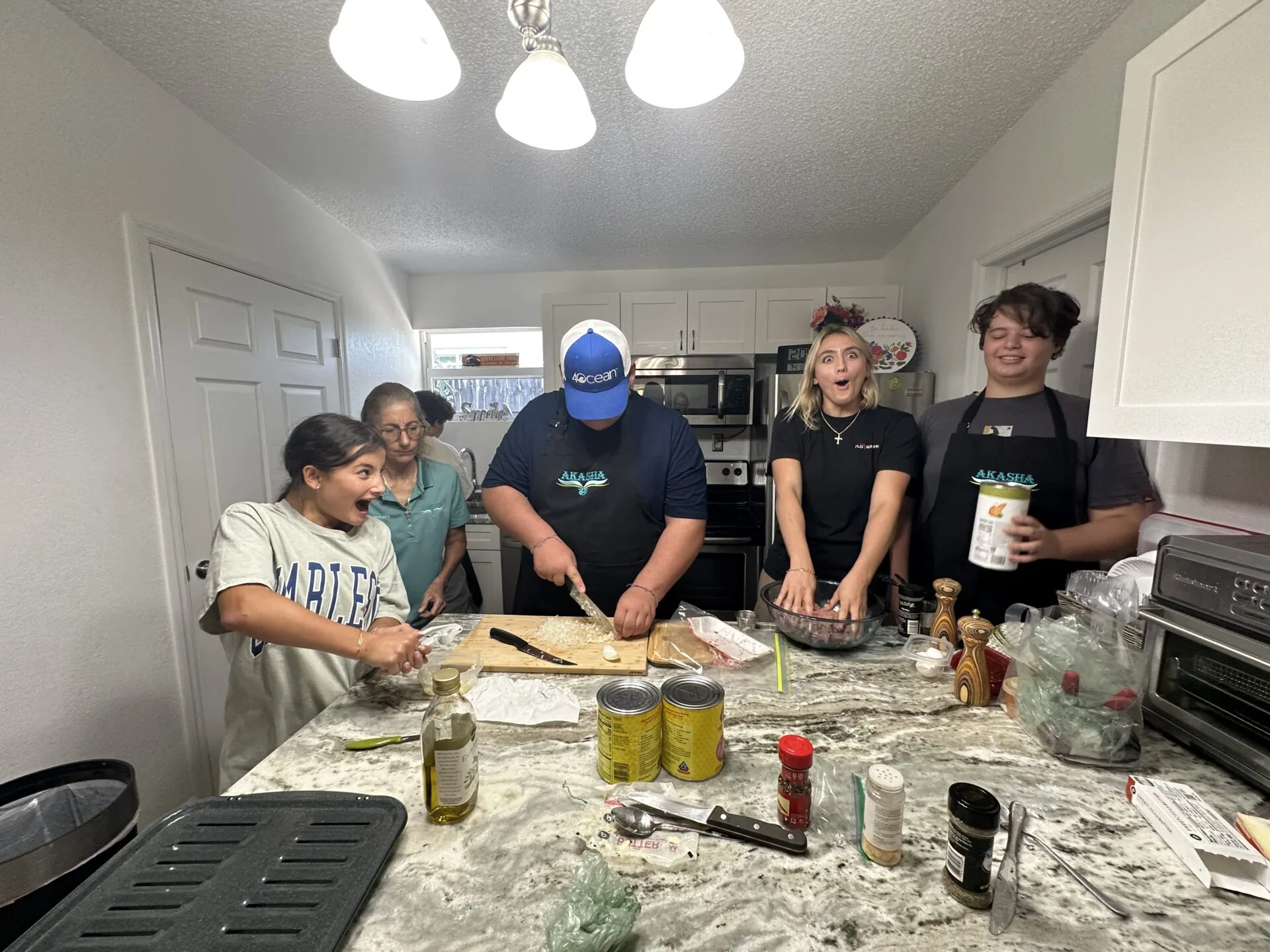 Group of six people gathered around a kitchen counter preparing food together