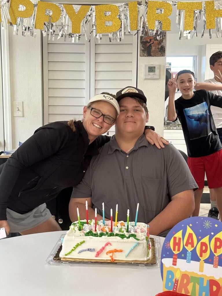 A teacher hugs a student behind a birthday cake full of candles