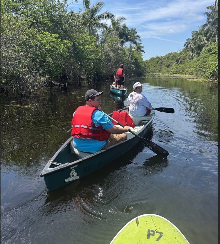 Students paddle a canoe down a calm, tree-lined river
