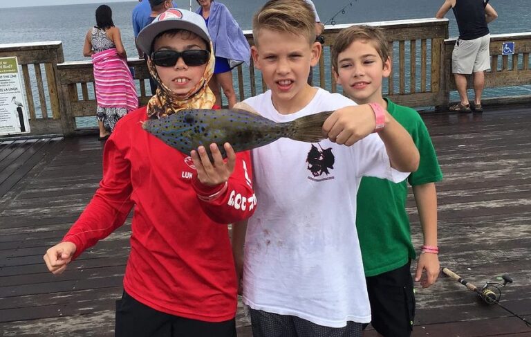 Three students on a fishing pier, one proudly holding up a fish
