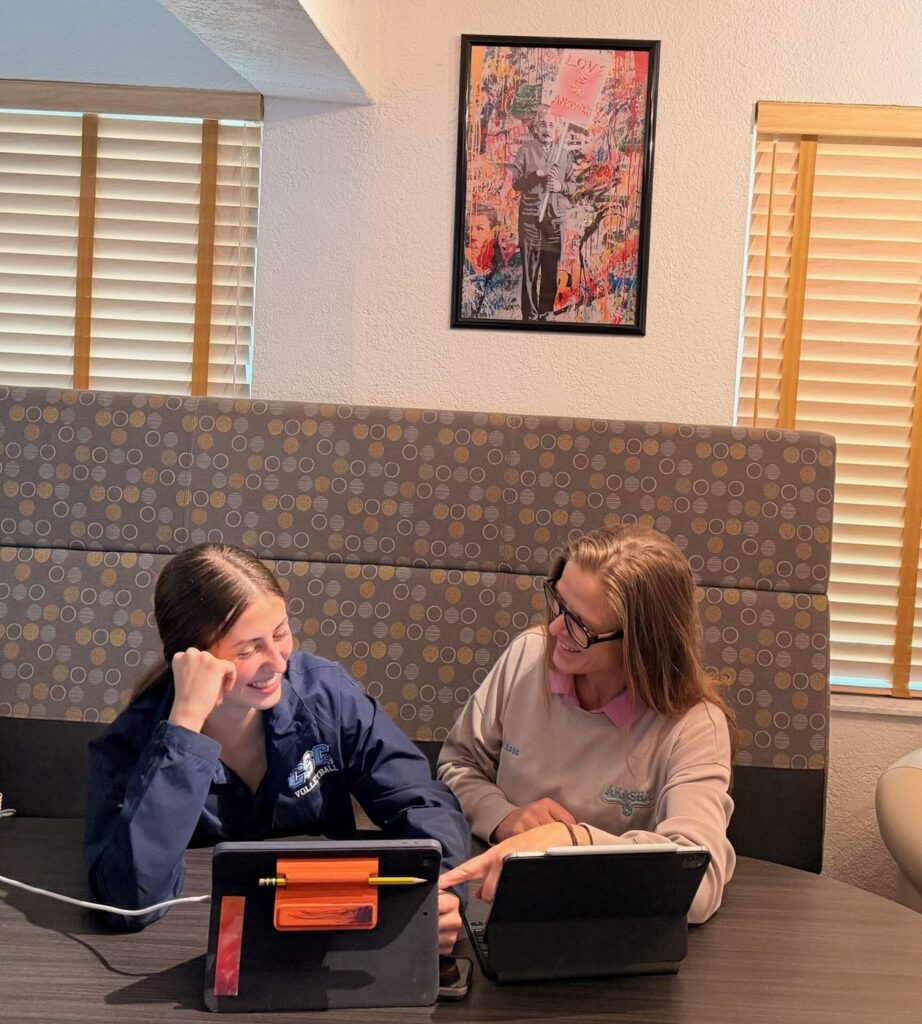 Two smiling students share a booth, each working on a tablet